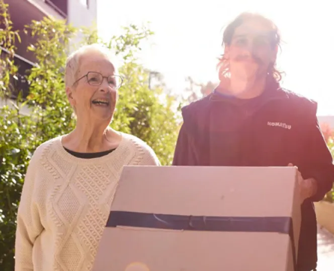 2 people smiling while moving boxes