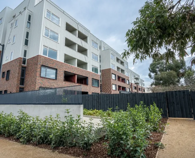A white and brick apartment building with a landscaped green open space and gravel pathway.