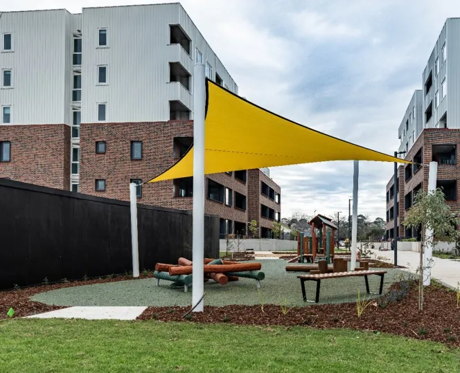 A children’s play equipment area next to paved walkways sitting between white and brick apartment buildings. 