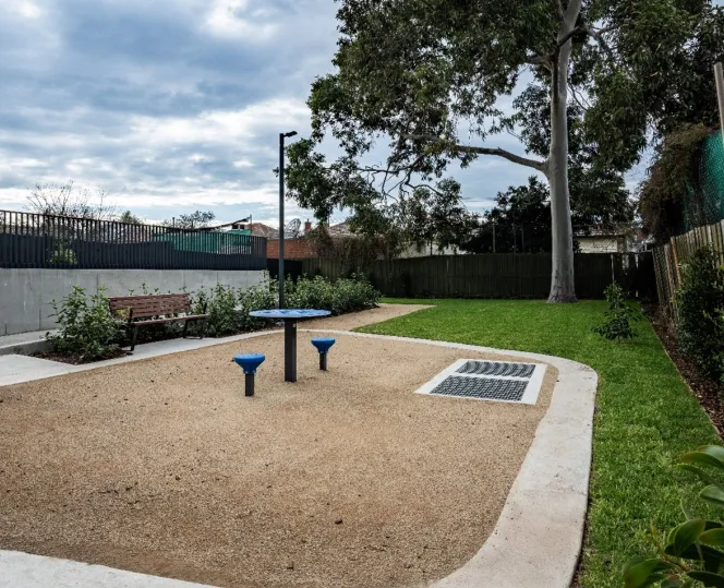 An outdoor chess table surrounded by open green space, landscaped greenery and seating.