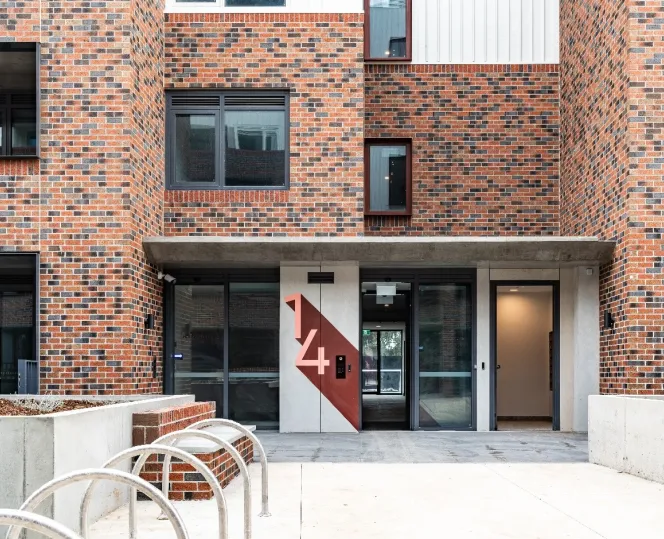 The lobby entrance of a brick building with a paved walkway leading inside and bike parking racks out the front.