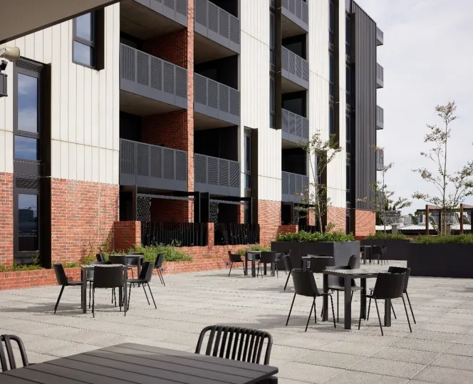 A paved courtyard with groups of tables and chairs. There is garden beds dotted around the area. 
