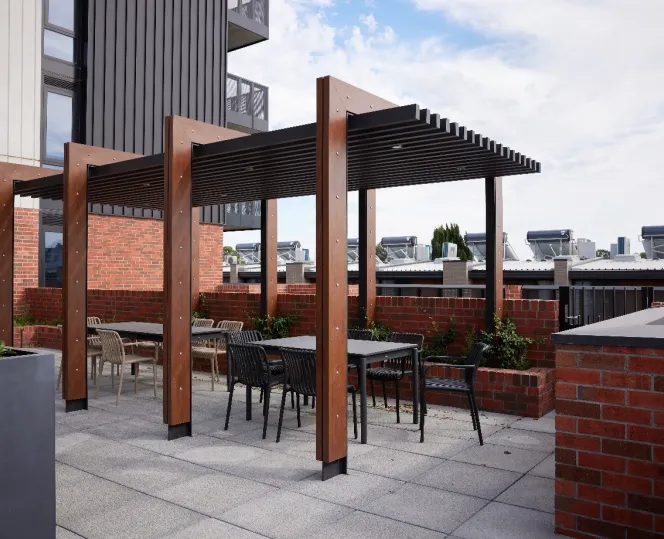 A section of a paved courtyard with an undercover seating area, barbeque and garden beds. 