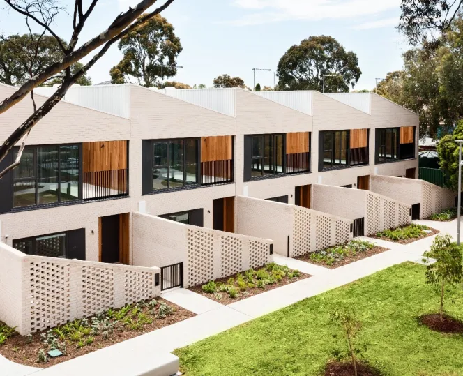 A row of apartments with landscaped gardens and pathways out the front of each one. 