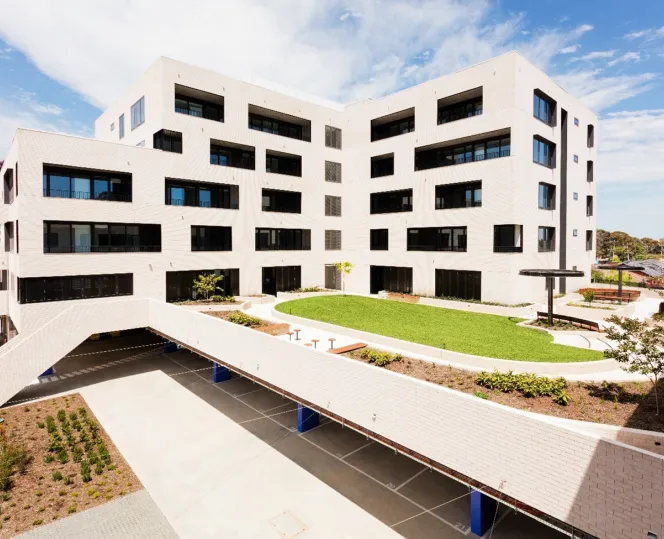 A large apartment building showing an open green space, landscaped gardens and carpark.