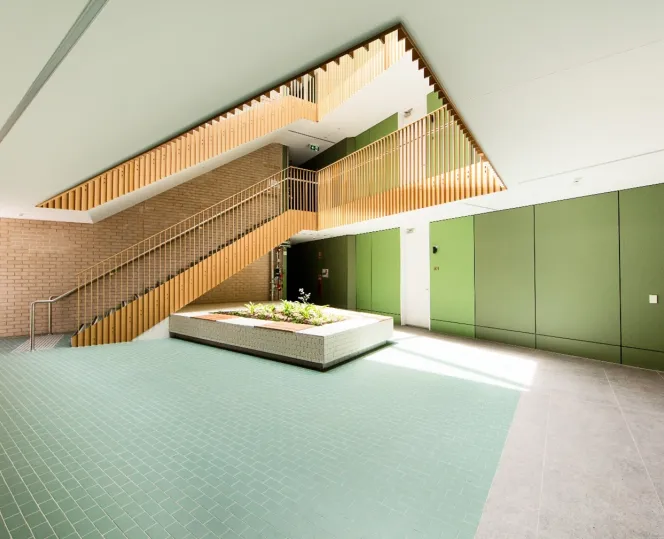 A brightly lit foyer and internal staircase decorated with green walls and blue floor tiling.