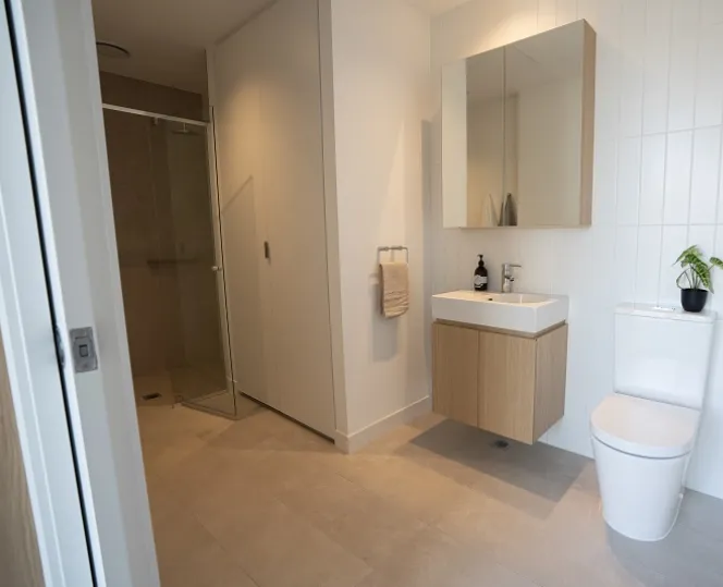 An image of the bathroom featuring a glass-enclosed shower and European laundry on the left, with the toilet and bathroom cabinetry on the right. 