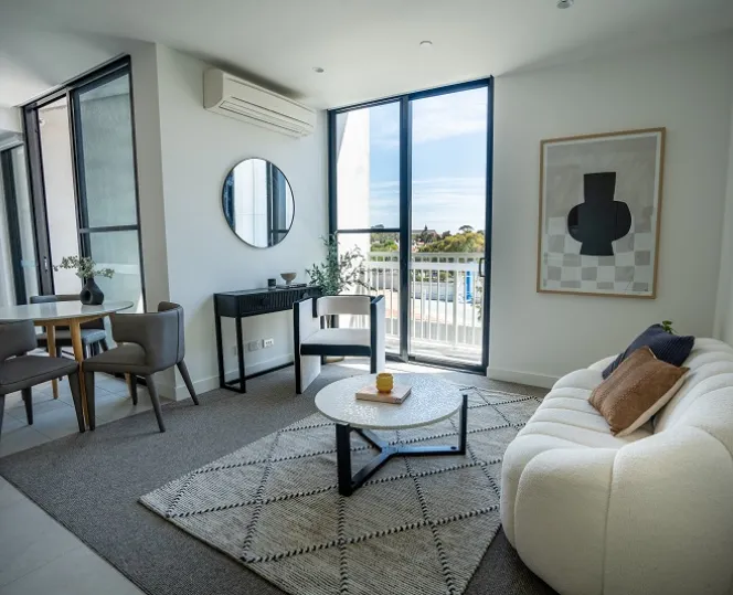 An image of the lounge room space inside a social housing apartment, furnished with a dining table, couch, and coffee table. 