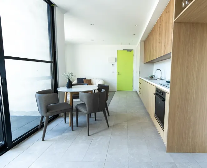 An image of the dining and kitchen area inside a social housing apartment, with a dining table on the left and the kitchen to the right. 