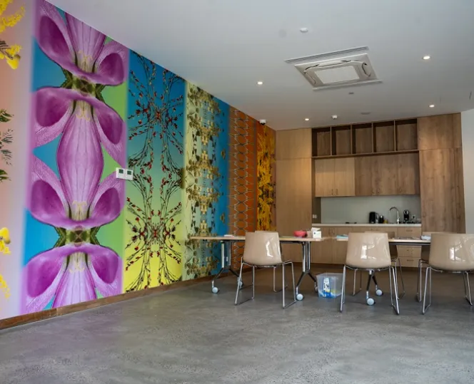 An image of the resident’s community room, featuring a kitchen area with décor, and a colourful wallpaper to the left showcasing Indigenous flora and fauna.  