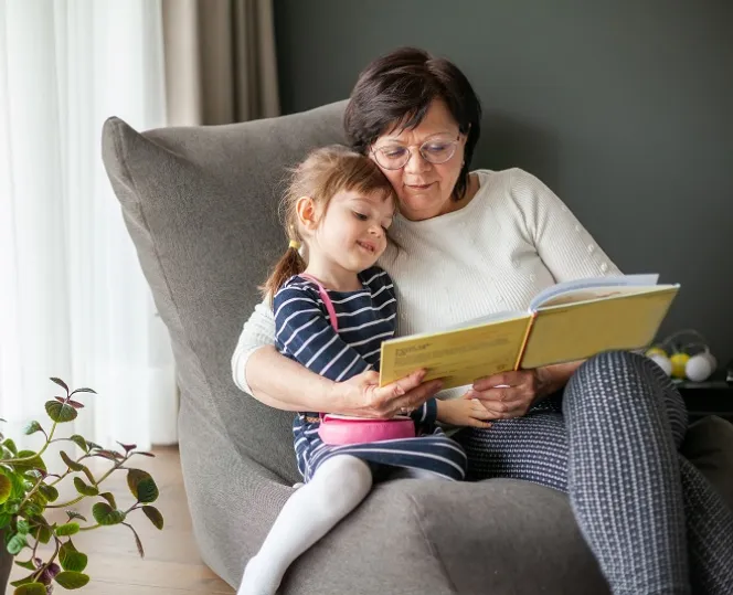 Image of a lady sitting on the chair with a child reading book for her