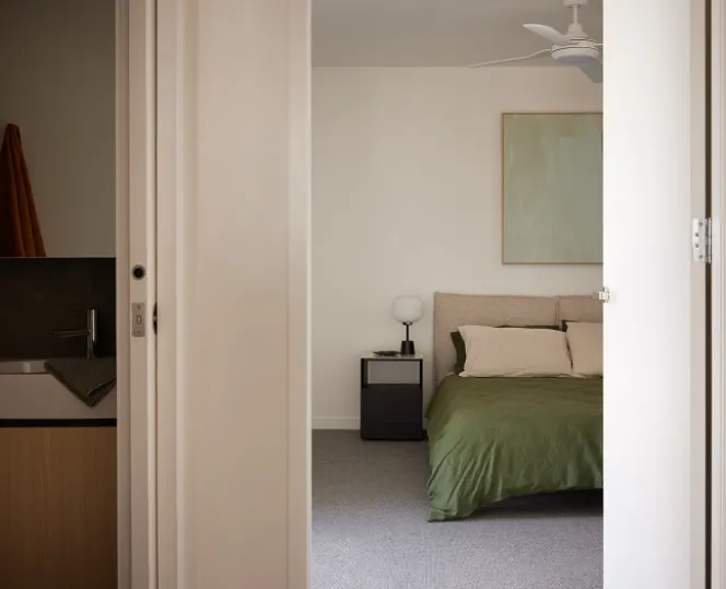 Inside the apartment showing a brightly lit bedroom including a green bed and the bathroom showing only a portion of the basin.  