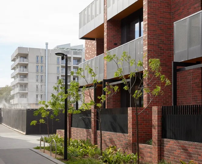 A brick apartment building with balconies and landscaped garden beds at the side boundaries of the building