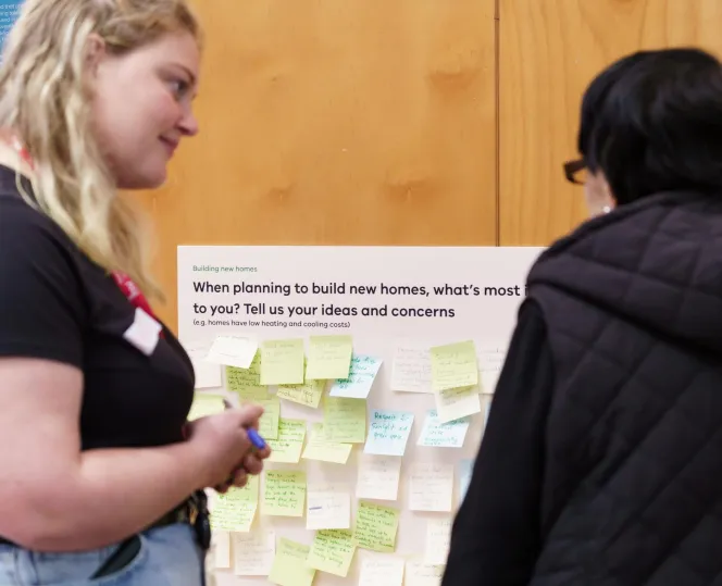 2 people talking in front of a board with sticky notes