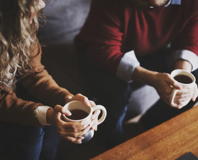 cropped image of 2 people sitting on a sofa with cups of coffee in their hands