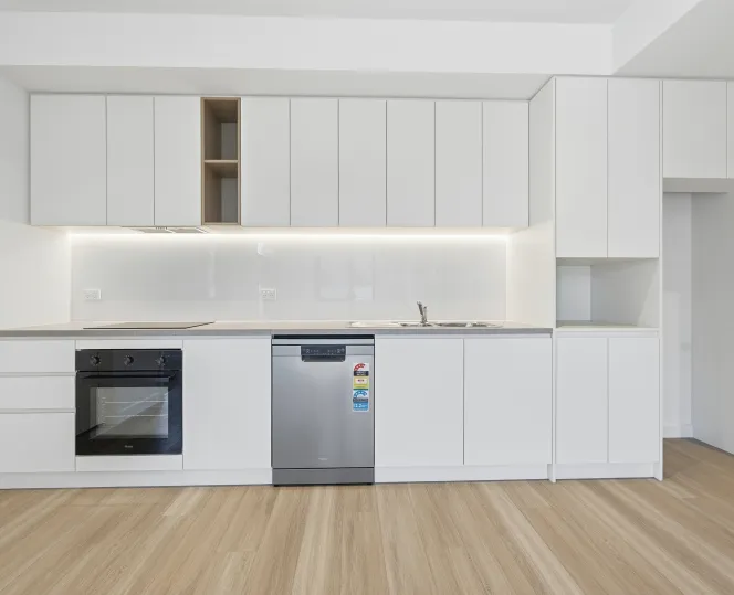 Modern kitchen with white cabinets, built-in oven and dishwasher, and clean counter tops.