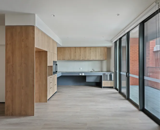 Modern kitchen with white cabinets, built-in oven, space for fridge, dishwasher, clean counter tops and big glass door for balcony