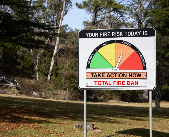 The photo shows a fire risk warning sign with an indicator set to Orange Extreme Risk 'Take Action now' and TOTAL FIRE BAN