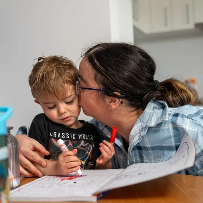 Image of a mother holding and kissing her toddler while they share a warm moment together.  
