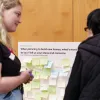 2 people talking in front of a board with sticky notes
