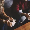 cropped image of 2 people sitting on a sofa with cups of coffee in their hands
