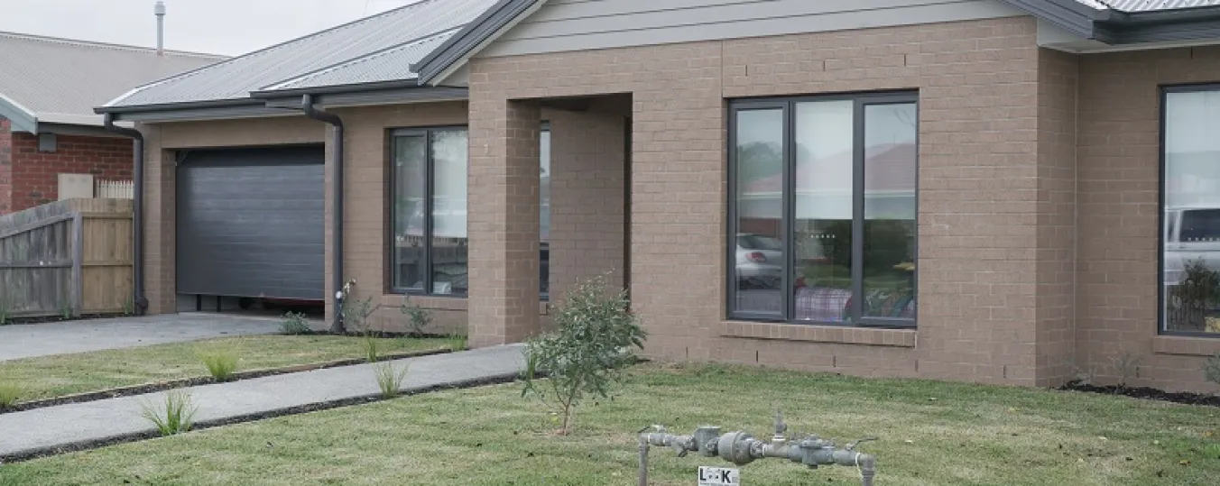 Image of house built with brown bricks having space for gardening in front  and garage space to park car