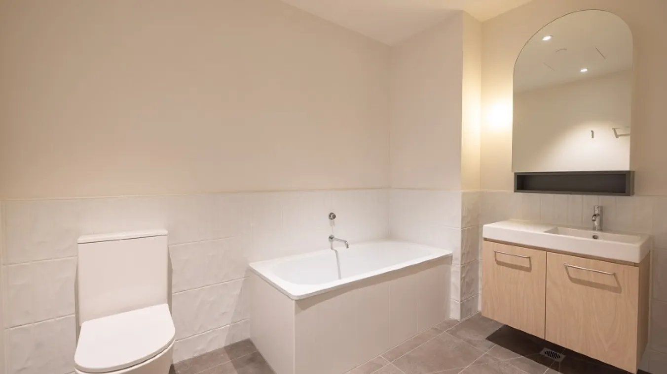 Image of modern bathroom interior featuring a white toilet, washbasin vanity, bathtub and a mirror.