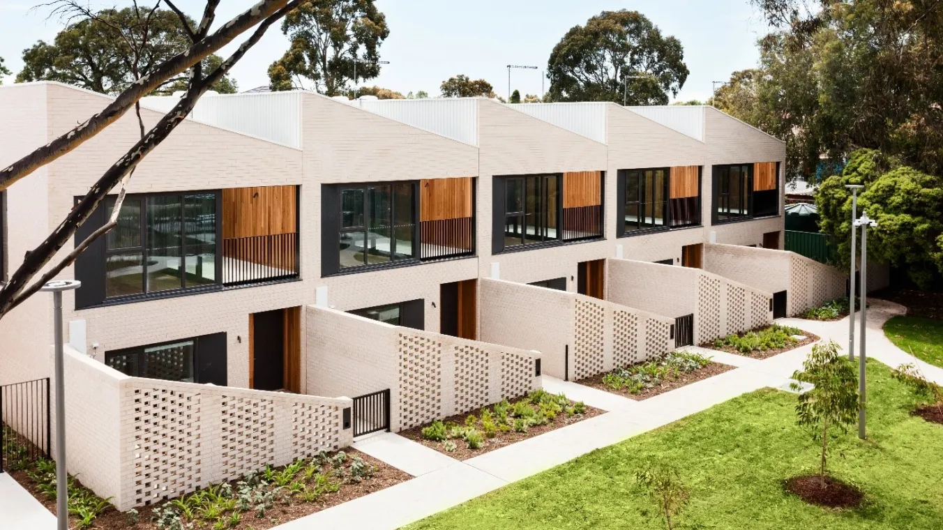 A row of apartments with landscaped gardens and pathways out the front of each one. 
