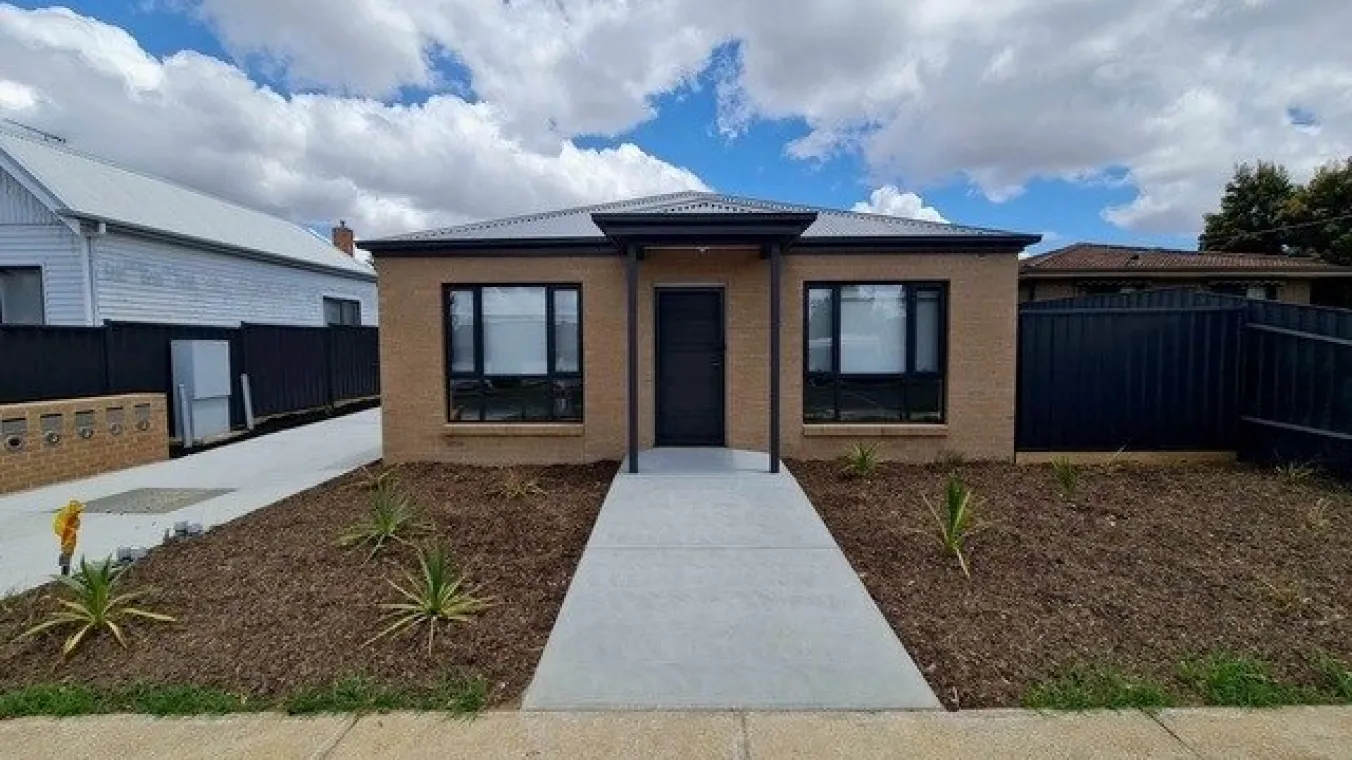 Image of house built with brown bricks having space for gardening in front  and garage space to par car
