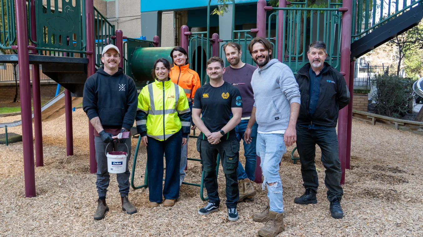 Group of tradespeople standing in front of playground equipment smiling to the camera
