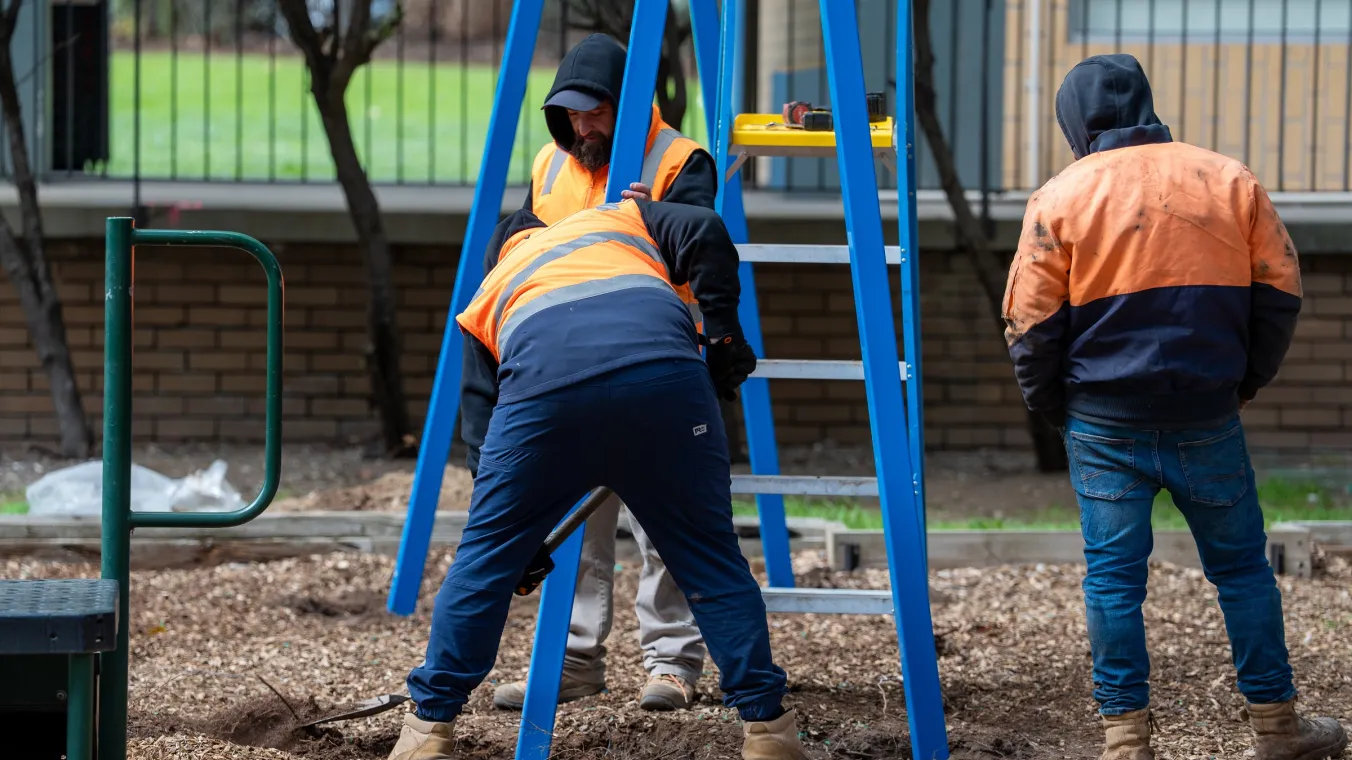 Tradespeople in high-vis installing playground equipment