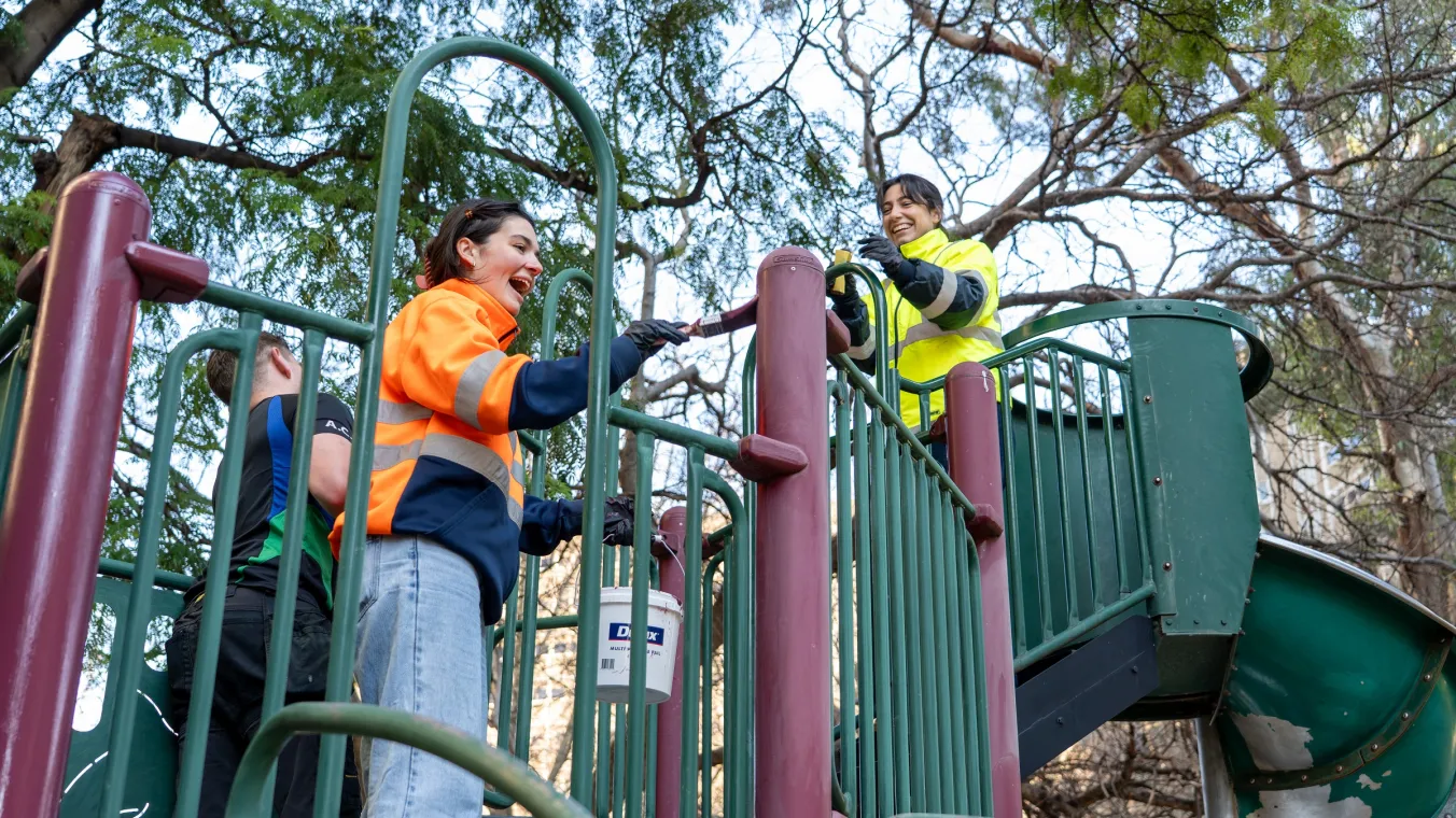 Tradespeople in high-vis painting playground equipment