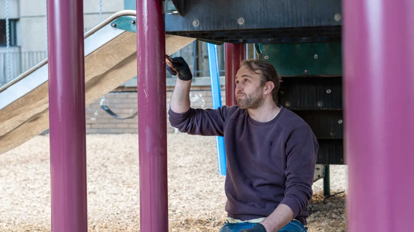 Trades-person on his knees painting playground equipment