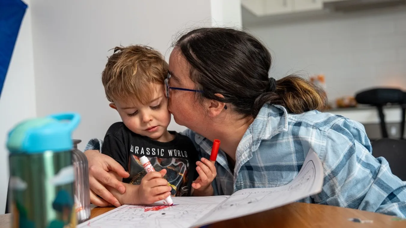 Image of a mother holding and kissing her toddler while they share a warm moment together.  