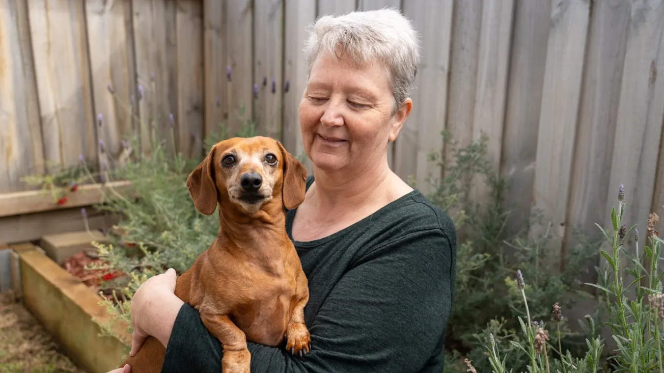 Image of  a woman smiling while holding her cute dog in her arms.