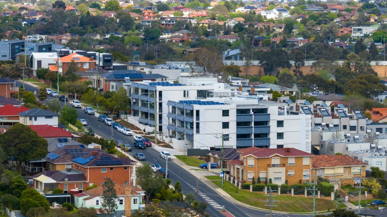 New social housing homes in Pascoe Vale, with neighbouring houses nearby and a road in front with a parked cars