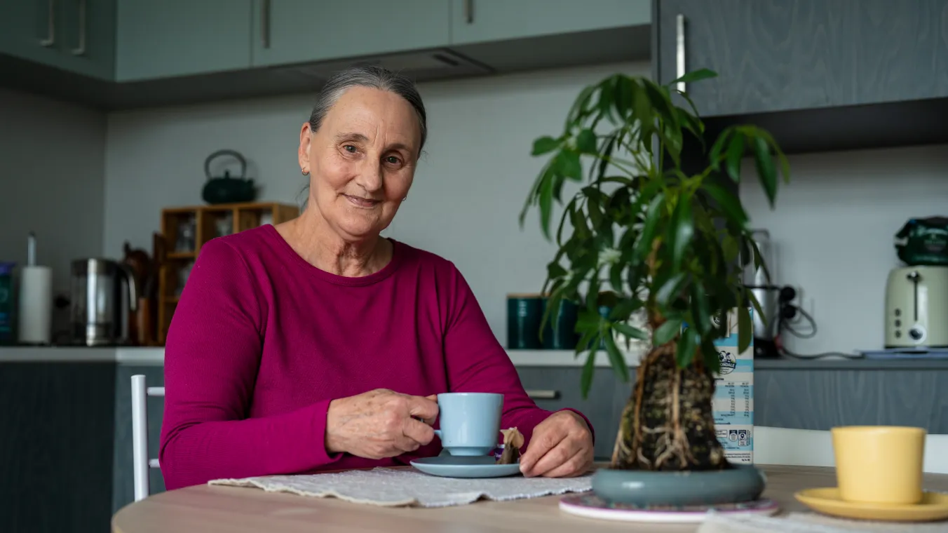 Image of a old lady sitting on her dinning table with a cup of tea