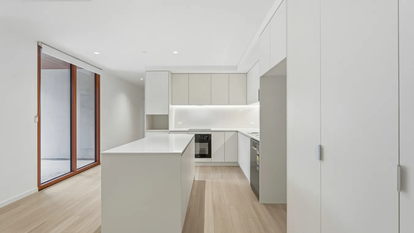 Kitchen with white cabinets for storage, an island benchtop and slidings doors to the outdoor balcony