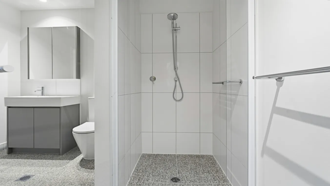 Inside a bathroom with a shower, toilet and mirrored vanity.