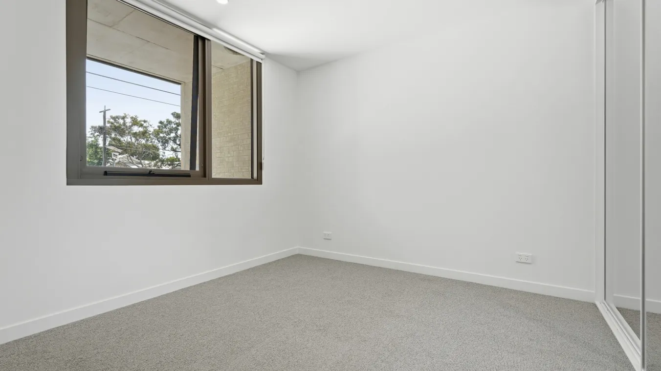 Bedroom with built-in mirrored wardrobes and large windows, creating a bright and functional space.