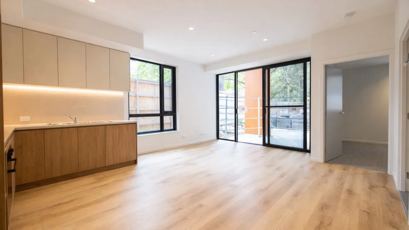 View from the front door across the kitchen and living area towards the balcony, with large windows and sliding doors bringing in natural light 