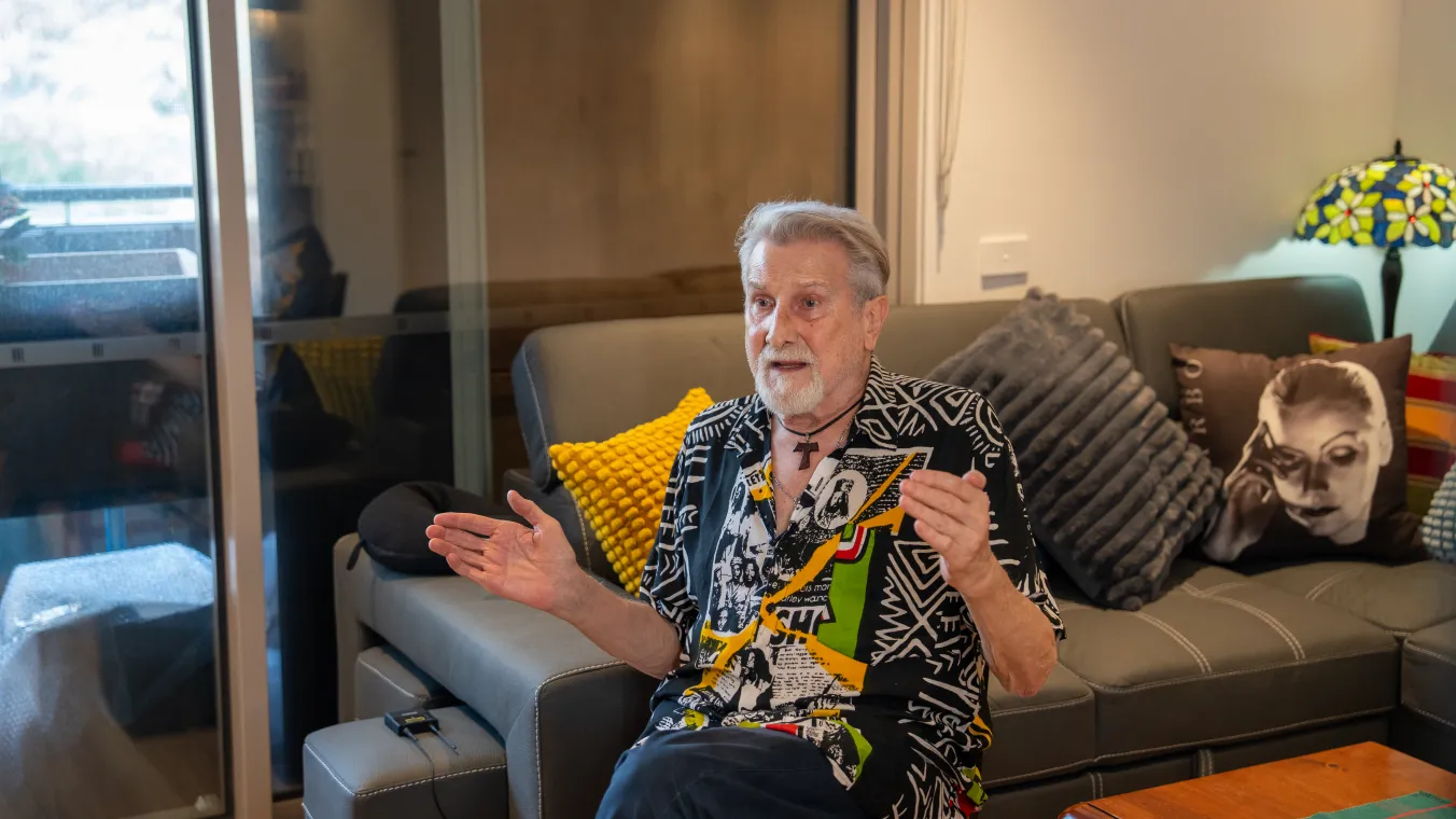 Image of man sitting on chair next to the couch and having conversation with the person interviewing him