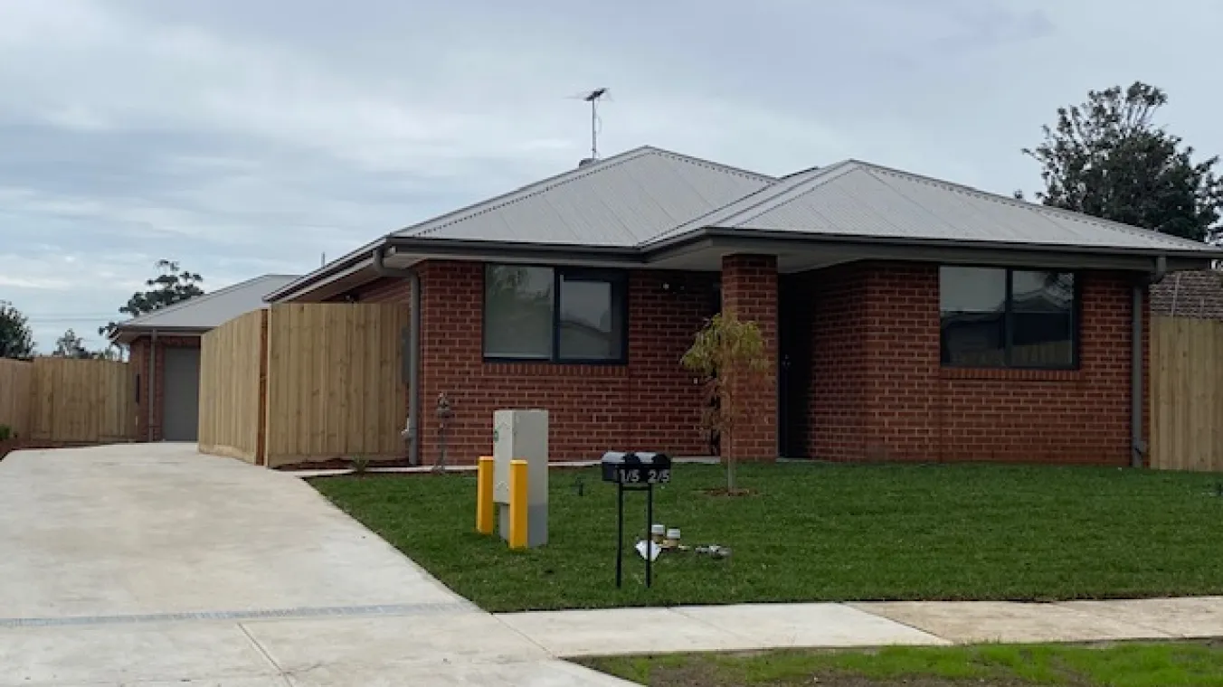 Image of a red brick house with a concrete driveway and landscaped garden at the front entrance.
