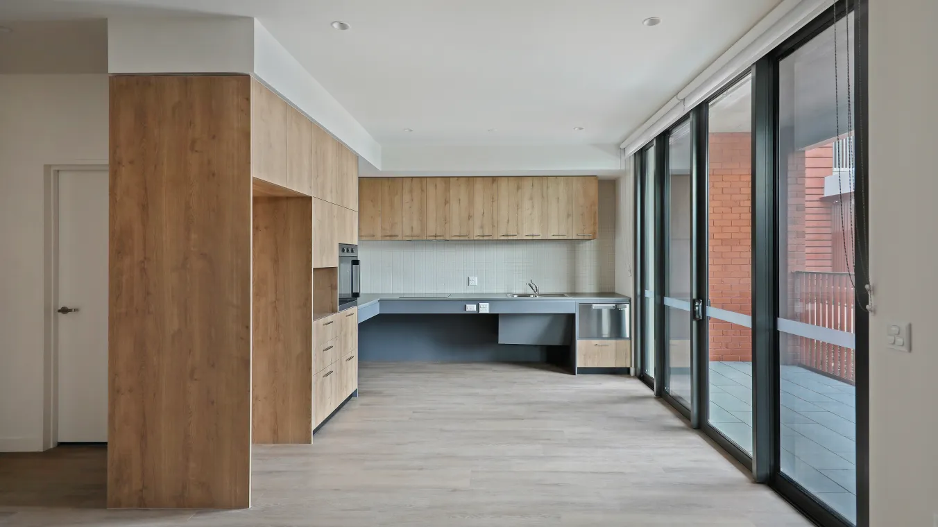 Modern kitchen with white cabinets, built-in oven, space for fridge, dishwasher, clean counter tops and big glass door for balcony