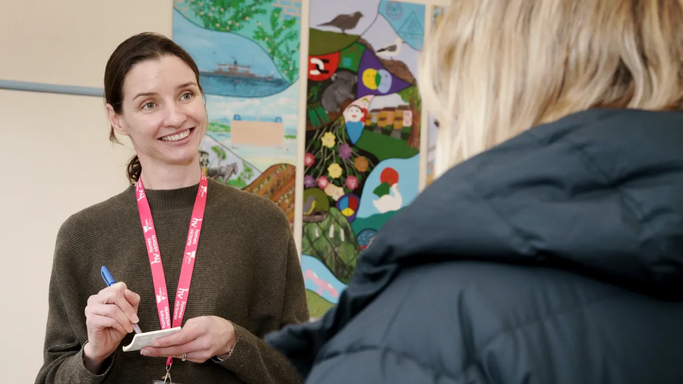 A woman smiling and taking a note while talking to another person