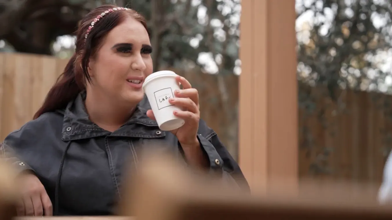 Young woman sitting in a garden drinking coffee from a take-away cup