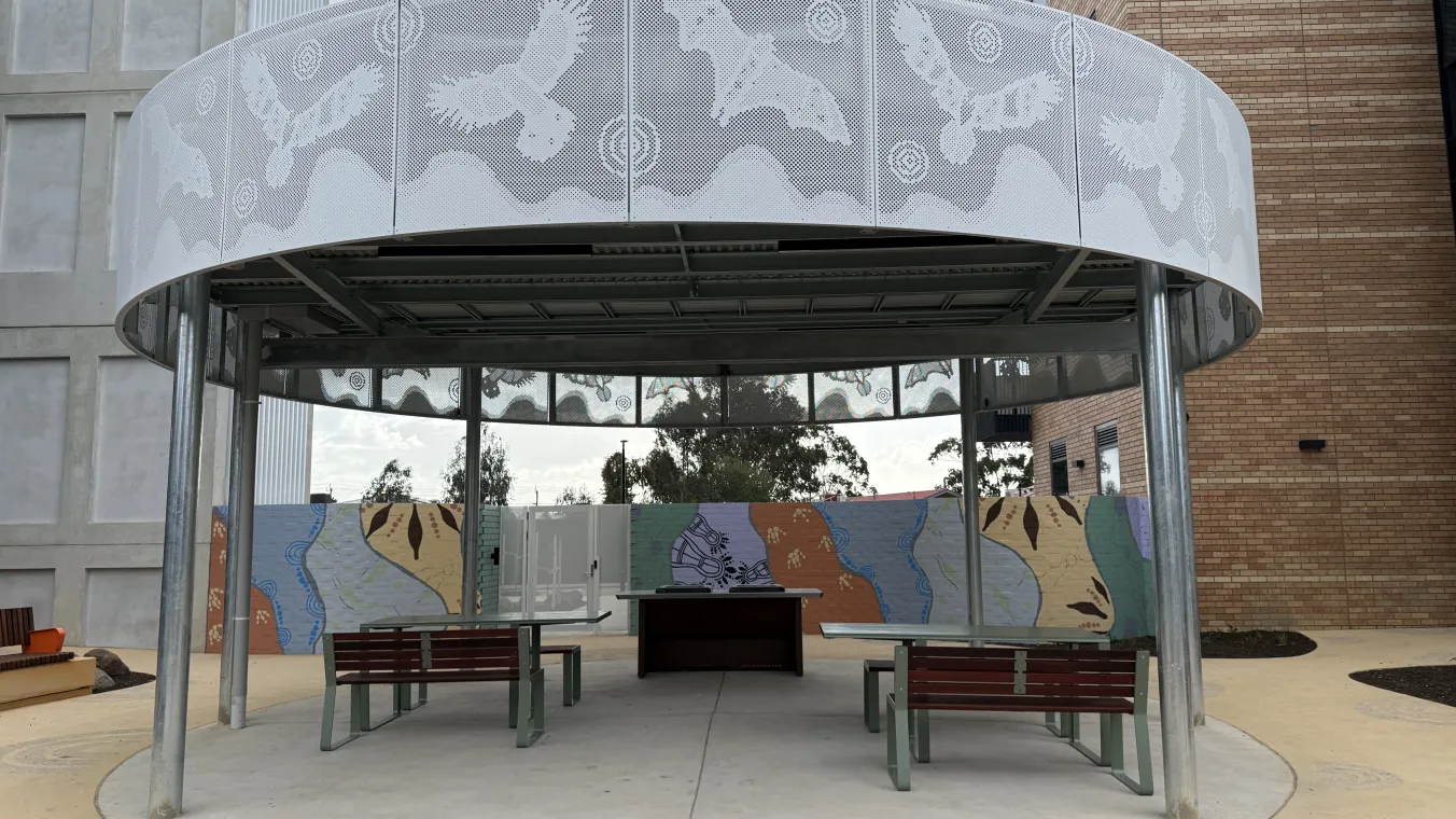 Barbecue area with a barbecue, bench seating and a shaded shelter featuring a mural design.  