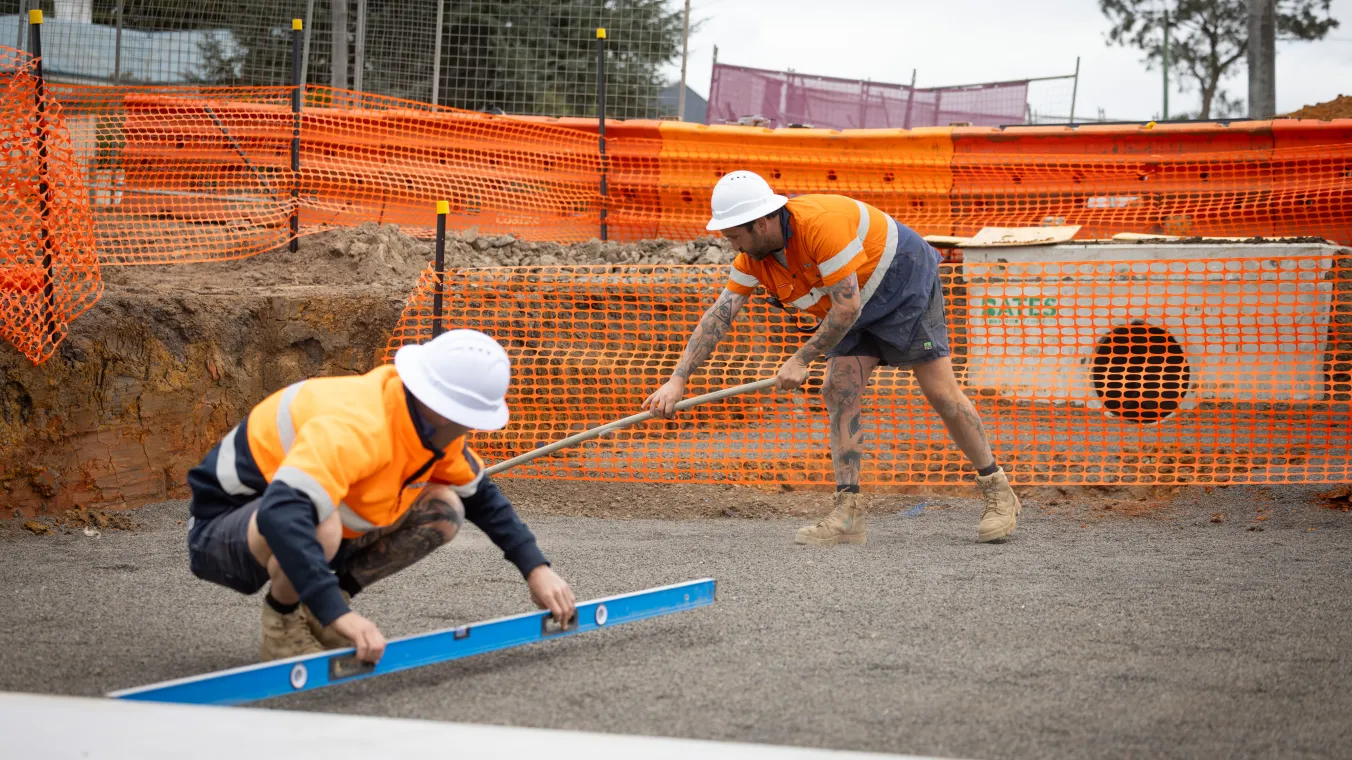 Construction workers wearing orange safety vests and white hard hats work at a construction site.