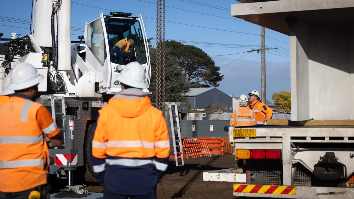 Construction workers wearing orange safety vests and white hard hats work at a construction site.
